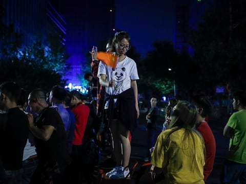A woman stands on a stool waves a Chinese national flag as residents watch the Chinese military vehicles move toward to Tiananmen Square in preparation for the parade for the 70th anniversary of the founding of the People's Republic of China, in Beijing, Tuesday, Oct. 1, 2019.