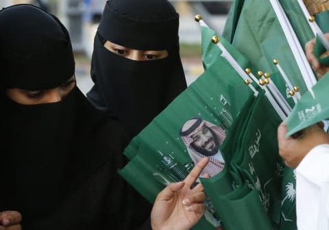 Women buy national flags with a picture of Crown Prince Mohammed bin Salman, marking National Day to commemorate the unification of the country as the Kingdom of Saudi Arabia, in Riyadh, Saudi Arabia, Monday, Sept. 23, 2019.