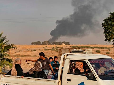 Civilians ride a pickup truck as smoke billows following Turkish bombardment on Syria's northeastern town of Ras Al Ain in the Hasakeh province along the Turkish border on October 9, 2019.