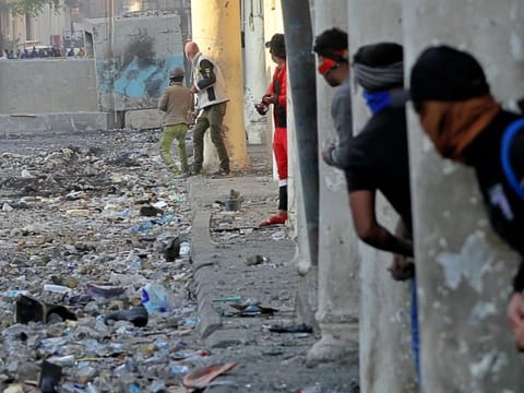 Demonstrators take cover during clashes between security forces and anti-government protesters in the historic Rasheed Street, Baghdad, Iraq, Sunday.