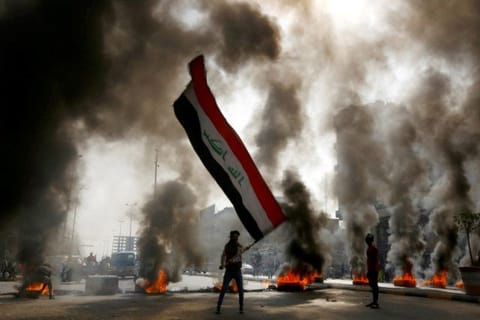 A protester holds an Iraqi flag amid a cloud of smoke from burning tires during ongoing anti-government protests in Najaf, Iraq.