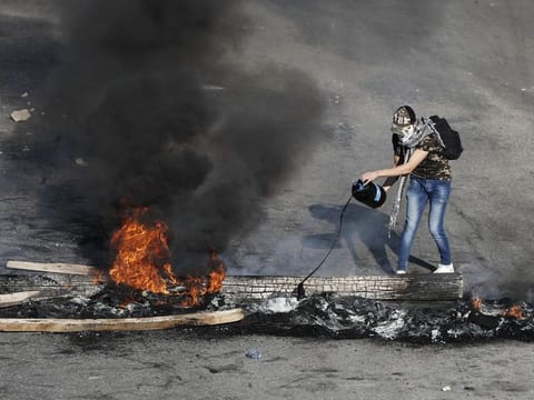 An anti-government protester drops oil on burning tires and wood during ongoing protests after weeks of calm in Beirut on Tuesday.