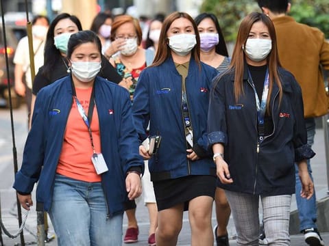 Office employees wearing facemasks walk along a street in Manila.