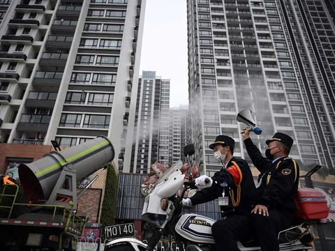 A man holding a loudspeaker sits on a motorcycle as it travels past a sanitising vehicle disinfecting the public space near residential buildings, following an outbreak of the novel coronavirus in the country, in Panyu district of Guangzhou, Guangdong province, China.