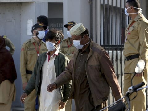 People and private guards wear masks while they gather outside a hospital, where victims of toxic gas leak, are treated in Kamari neighborhood of Karachi on Monday.