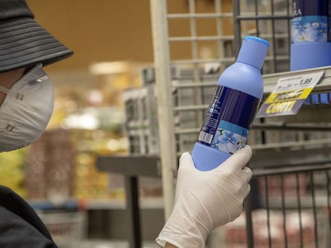 A customer wearing a protective face mask and gloves reads a cleaning product label in a grocery store in Milan, Italy, on Tuesday, Feb. 25, 2020.