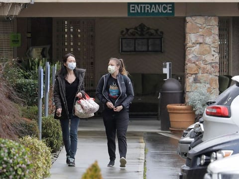 Two women wearing masks walk away from the Life Care Center in Kirkland, Wash., near Seattle, Monday, March 2, 2020.