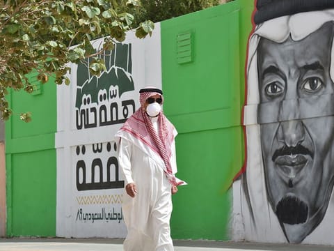 A Saudi man, wearing a protective mask as a precaution against COVID-19 coronavirus disease, walks past a mural showing the face of King Salman bin Abdulaziz, along Tahlia street in the centre of the capital Riyadh