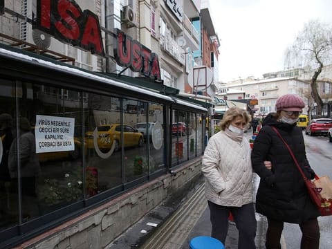Face-masked people walk past closed restaurants, in Ankara, Turkey, Thursday, March 19, 2020.