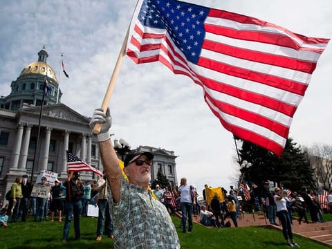 A man waves a US flag in front of the Colorado State Capitol building during a demonstration to protest coronavirus stay-at-home orders at a "ReOpen Colorado" rally in Denver, Colorado, on April 19, 2020.
