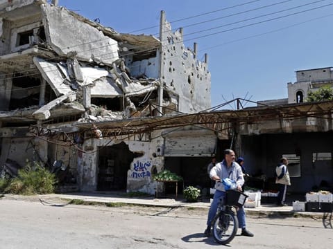 Syrians sells vegetables next to buildings heavily damaged during Syria's civil war, in the central city of Homs, on April 28.