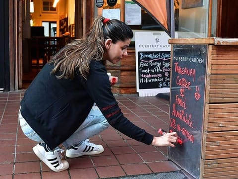 A woman writes on a signboard outside her cafe on the first day of the easing of restrictions in Wellington on April 28, 2020, following the COVID-19 coronavirus outbreak.