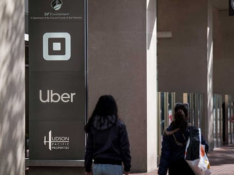 Pedestrian pass in front of signage displayed outside Uber Technologies headquarters in San Francisco, California.