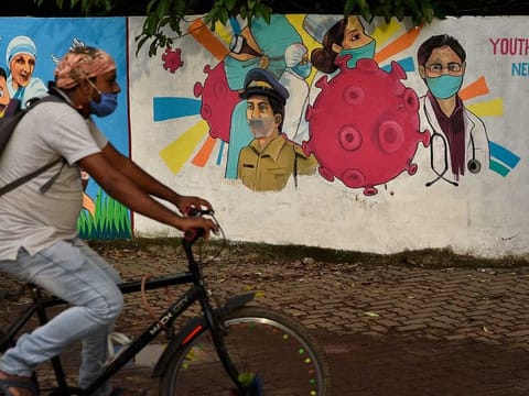 A man wearing a mask pedals his bicycle past a graffiti on a wall made to create awareness about the coronavirus in Kochi, Kerala state, India, Thursday, June 11, 2020.