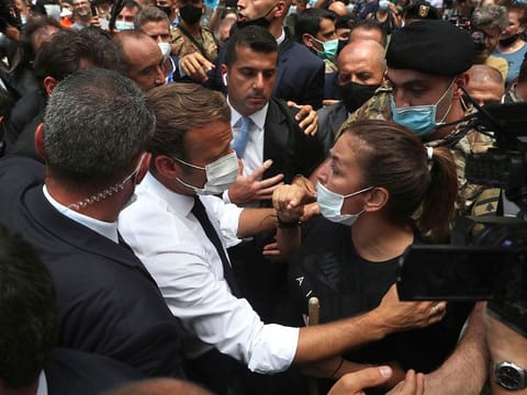 French President Emmanuel Macron, speaks with a woman as he visits the Gemayzeh neighborhood, which suffered extensive damage from an explosion on Tuesday that hit the seaport of Beirut