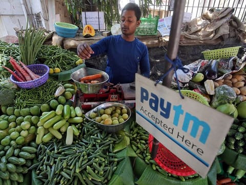 A vendor weighs vegetable next to an advertisement of Paytm, a digital payments firm, hanging amidst his vegetables at a roadside market in Mumbai, India.