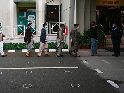 A police officer (R) checks the body temperature of people entering the Supreme Court building in Islamabad on November 25, 2020.