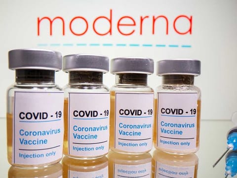 Vials with a sticker reading, "COVID-19 / Coronavirus vaccine / Injection only" and a medical syringe are seen in front of a displayed Moderna logo in this illustration taken October 31, 2020.