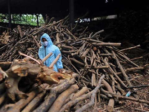 A worker wearing personal protection equipment (PPE) loads wood onto a cart at a crematorium on the outskirts of New Delhi, India, on Friday, April 23, 2021.
