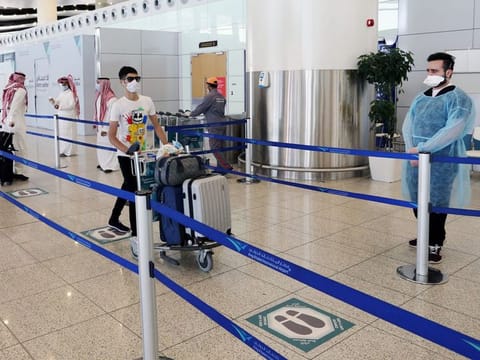 A traveller wearing a protective face mask wheels his bags at Riyadh International Airport, in Riyadh, Saudi Arabia