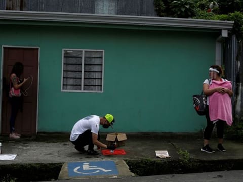 A worker sprays paint on a stencil indicating social distancing on the floor of a bus stop, as the spread of the coronavirus disease continues, in San Jose, Costa Rica.