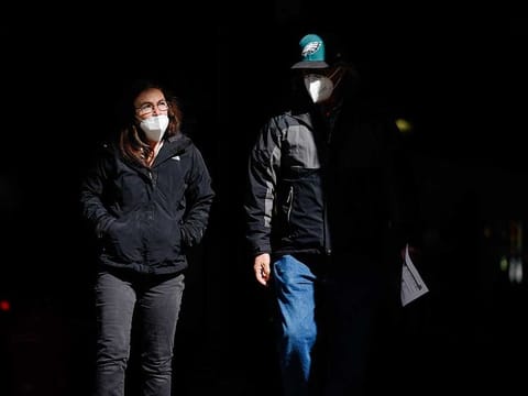In this Wednesday, March 3, 2021 file photo, people wearing face masks as a precaution against the coronavirus walk through a shaft of light on a street in Philadelphia.