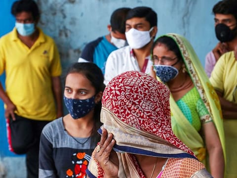 People wearing masks wait to test for COVID-19 at a hospital in Hyderabad, India.