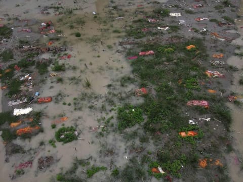 The risen water level of the Ganges River washes away the sparse layer of the soil revealing the shallow graves of suspected Covid-19 coronavirus deaths and other fatalities wrapped in cloth at the Phaphamau ghat near a cremation ground in Allahabad on June 27, 2021.