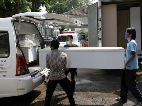 Workers wearing protective masks load coffins for COVID-19 victims into an ambulance to be distributed to a hospital in Jakarta, on July 5, 2021.