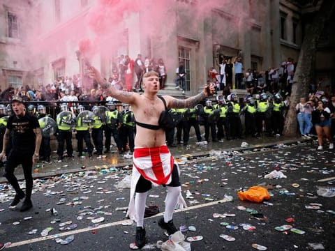 An England fan waves a smoke bomb in front of a line of police officers monitoring England supporters standing on the edge of Trafalgar Square during a live screening of the Euro 2020 football final between England and Italy, in central London on July 11, 2021.