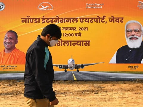 A man walks past a hoarding during an event to lay the foundation stone of the Noida International Airport at Jewar in Uttar Pradesh on November 25, 2021.