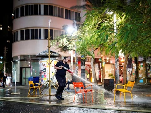 A man sprays water to clean chairs and a street, as Israel imposes a third national lockdown to fight climbing coronavirus disease (COVID-19) infections, in Tel Aviv, Israel December 27, 2020.