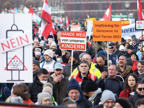 People demonstrate with placards reading "Hands off our children" and at (right) "Compulsory vaccination for recovered people is Nazi-terror 2021" against the Austrian government's measures taken in order to limit the spread of the COVID-19 during a protest in Vienna on January 8, 2022.