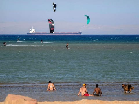 Egyptian holiday-makers enjoy the beach as a cargo container ship, crosses the Gulf of Suez towards the Red Sea at al Sokhna beach in Suez, 127 kilometres east of Cairo, Egypt, Friday, Aug.26, 2022.