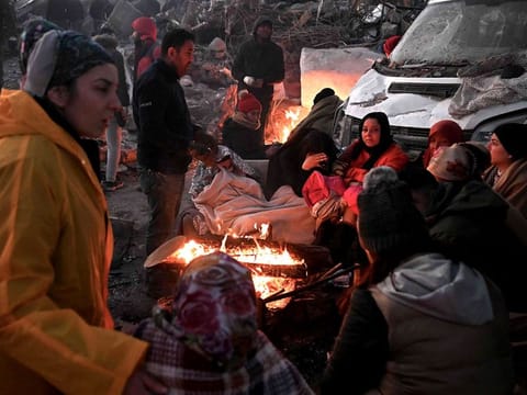 People warm themselves near a bonfire amidst the rubble of collapsed buildings in Kahramanmaras, Turkey, on February 8, 2023, two days after a 7,8-magnitude earthquake struck southeast Turkey. Searchers were still pulling survivors on from the rubble of the earthquake in Turkey and Syria, even as the window for rescues narrowed.