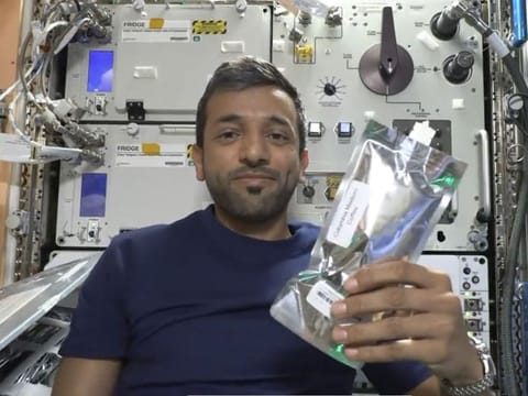 Still from clip of Al Neyadi with a coffee pouch on ISS