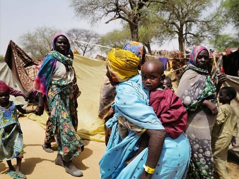 A sudanese woman who fled the conflict in Sudan's Darfur region, carries a child as she walks past makeshift shelters near the border between Sudan and Chad, while taking refuge in Borota, Chad, on May 13, 2023.
