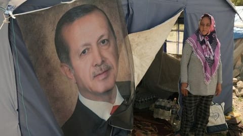 Ayse Kekec, an earthquake survivor living in a tent with her son, stands in front of their tent with a poster of Turkish President Erdogan on it, in Kahramanmaras, Turkey May 11, 2023.
