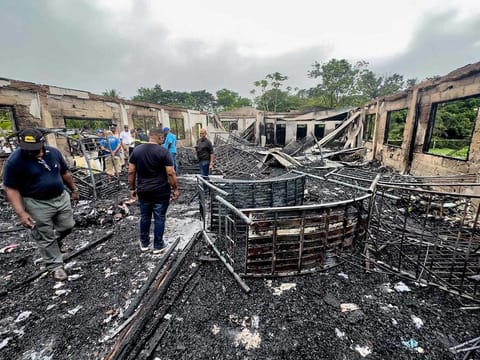 Investigators and government employees inspect the school dormitory where a fire killed at least 20 people in Mahdia, Guyana on May 22, 2023.