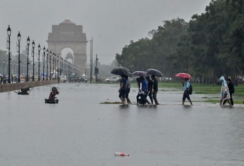People cover their heads with umbrellas as they wade through waterlogged streets at India Gate during heavy rainfall, in New Delhi on Sunday, July 9, 2023.