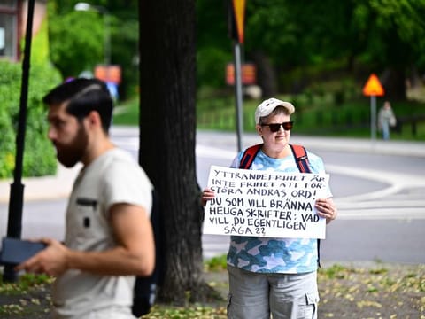 A woman with a protest poster stands next to Ahmad A. (left) who has been given permission by the police for a public gathering to burn a Torah and a Bible outside the Israeli embassy in Stockholm, Sweden, on July 15, 2023.