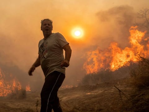 A local reacts as the flames burn trees in Gennadi village, on the Aegean Sea island of Rhodes, southeastern Greece.