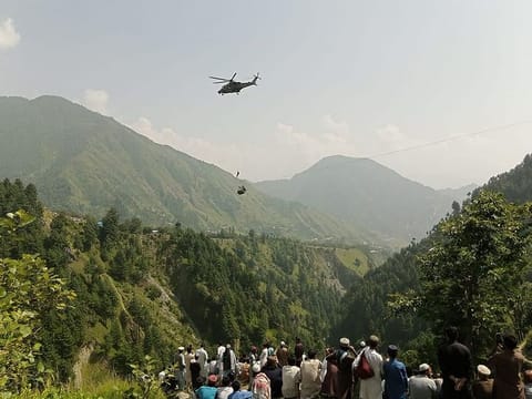 People watch as an army soldier slings down from a helicopter during a rescue mission to recover students stuck in a chairlift in Pashto village of mountainous Khyber Pakhtunkhwa province, on August 22, 2023.