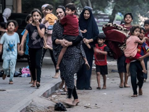 Women and children, barefoot, are seen evacuating along a street in Gaza City, seeking safety amidst the escalating Israeli airstrikes