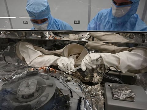 Scientists use tools to collect asteroid particles from the base of a canister.