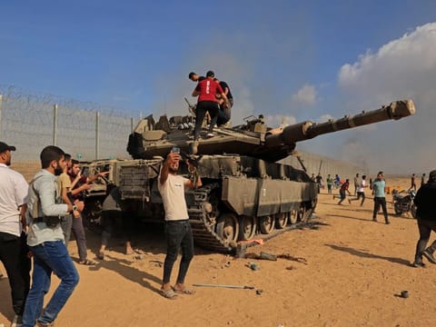 Palestinians take control of an Israeli Merkava battle tank after crossing the border fence with Israel from Khan Yunis in the southern Gaza Strip on October 7, 2023.