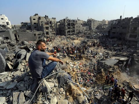A man sits on the rubble as others wander among debris of buildings that were targeted by Israeli airstrikes in Jabaliya refugee camp, northern Gaza Strip on November 1, 2023.
