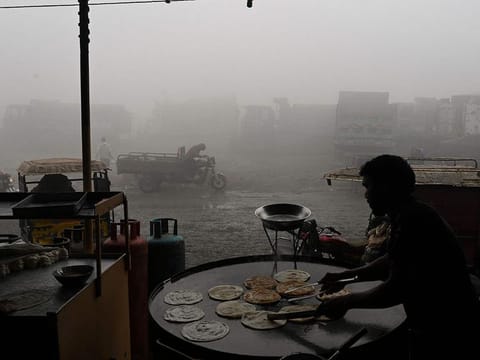 A man makes bread along a road amid heavy smog in Lahore on December 14, 2023.
