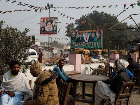 People sit outside a tea stall with billboards of political leaders in the background, ahead of the general elections in Larkana, Pakistan, on January 16, 2024.