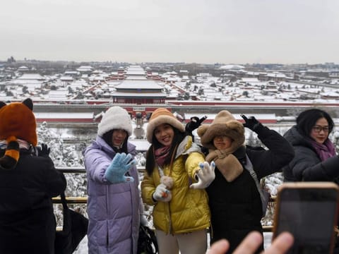 In this photo released by Xinhua News Agency, visitors pose for a photo with the Forbidden City in the background at Jingshan Park following a snowfall in Beijing, on February 21, 2024.